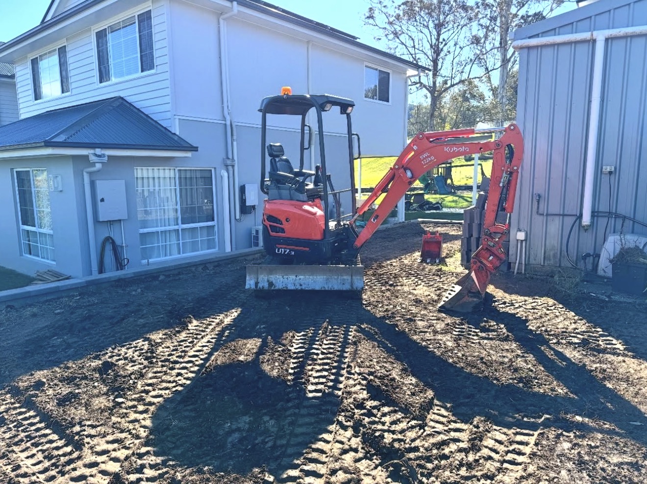Kubota excavator executing residential site cut and soil levelling beside house